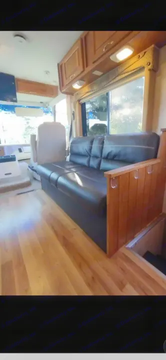Spacious RV rental interior featuring a dark sofa, light wood floors, overhead cabinetry, and the front driving area.. Ford 1F6NF3S740A06630 2004