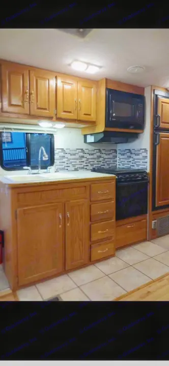 RV rental kitchen features light oak cabinets, mosaic backsplash, sink, black microwave, oven, and tiled floor.. Ford 1F6NF3S740A06630 2004