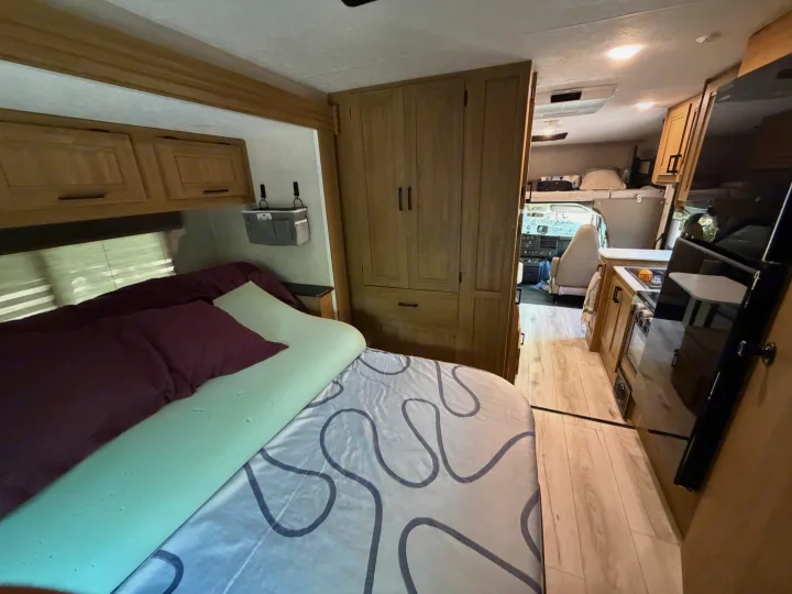 RV rental interior, showcasing the bedroom with topper, built-in storage, kitchen, and front driving area.. Coachman Leprechaun 2025