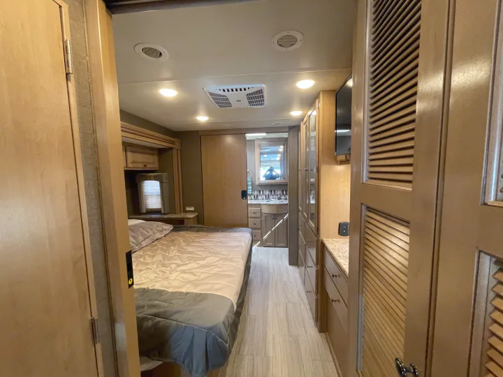 Modern RV rental interior: A comfortable bedroom leads to a hallway with storage, a wall-mounted TV, and a bathroom vanity.. Thor Windsport 2019