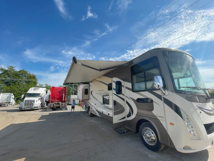 This Thor Windsport RV rental features an extended awning, parked on a sunny lot alongside semi-trucks.. Thor Windsport 2019