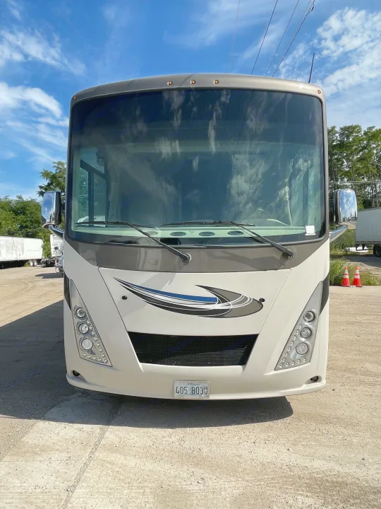 Front view of a modern beige and gray RV for rent. This spacious motorhome features large headlights and a blue graphic on the grille.. Thor Windsport 2019