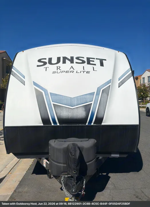 Front view of an RV rental: a white Sunset Trail Super Lite travel trailer with blue and gray graphics under a clear sky.. Crossroads RV Sunset Trail Super Lite 2021