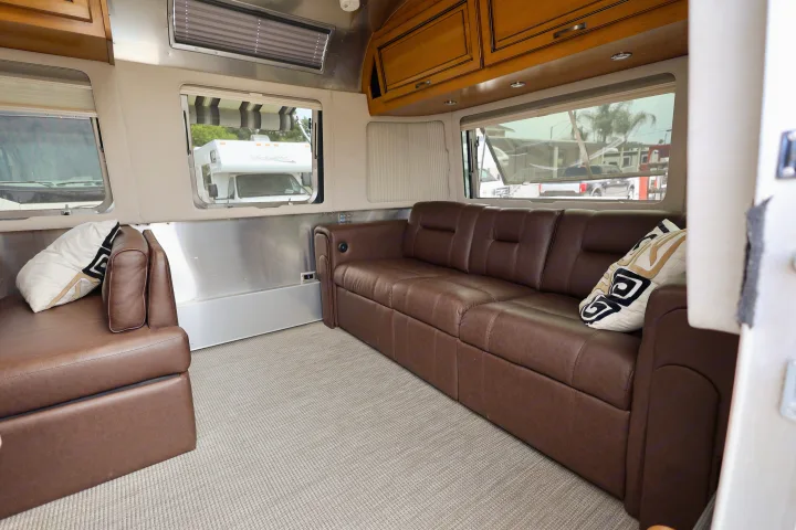 Comfortable RV rental interior featuring brown leather sofas, large windows, wooden cabinets, and a light-colored carpet.. Airstream Classic 2019
