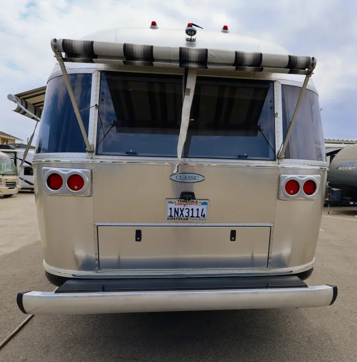 Rear of a silver Airstream Classic RV rental, featuring its iconic design, large windows, rolled-up awning, and red taillights.. Airstream Classic 2019