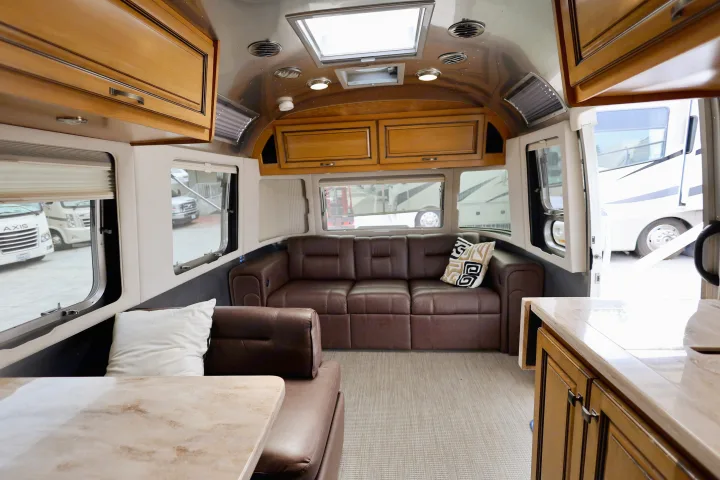 Curved interior of an RV rental with brown leather sofa, wood cabinets, light countertop, and scenic window views.. Airstream Classic 2019