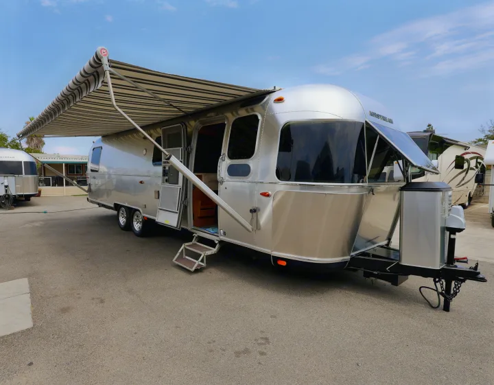 Silver Airstream travel trailer RV rental with awning extended, door open, and steps down, parked on asphalt.. Airstream Classic 2019