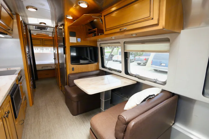 Discover this spacious RV rental interior: dining booth, TV, kitchen, and glimpse of the bedroom area.. Airstream Classic 2019