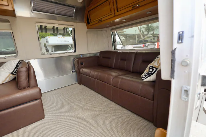 Spacious rv rental interior showing brown leather sofas, wood cabinets, and large windows with outdoor views.. Airstream Classic 2019