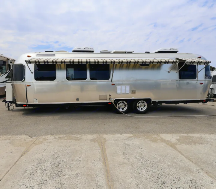 Shiny silver Airstream Classic RV rental, awnings extended, parked on pavement under a cloudy sky.. Airstream Classic 2019