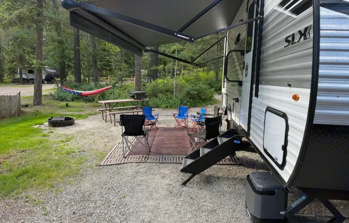 A cozy RV rental campsite nestled in the woods, featuring an extended awning, comfy chairs, a picnic table, grill, and a patriotic hammock.. Jayco Jay Flight SLX Baja Edition 2025