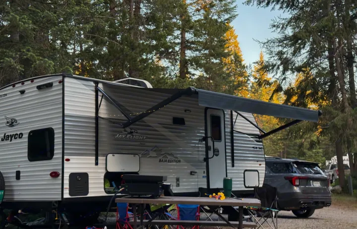 Jayco rv rental at a peaceful campsite with extended awning, grill, and picnic table. Pine trees in the background.. Jayco Jay Flight SLX Baja Edition 2025
