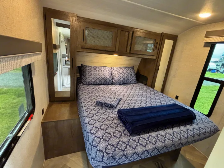 This cozy RV rental bedroom features a patterned bed, storage cabinets, and large windows, perfect for comfortable travel.. Forest River Wildwood 2021