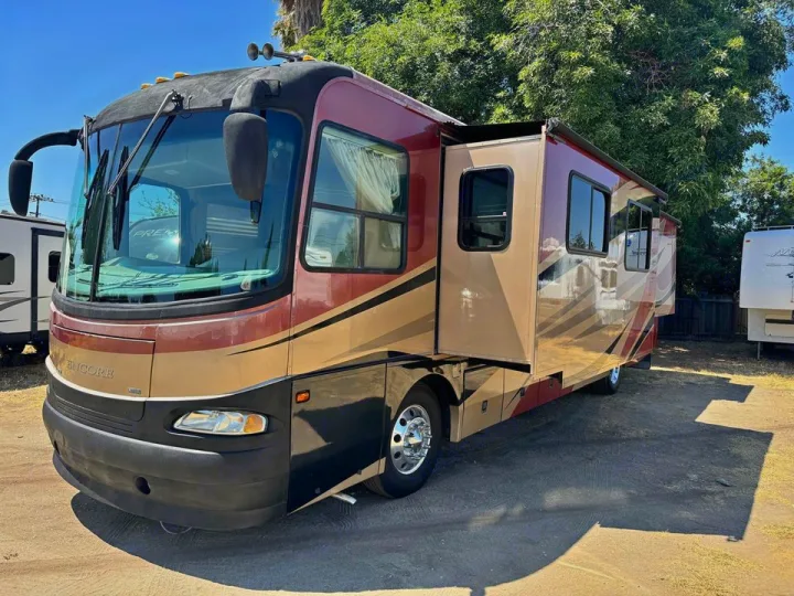 A large maroon and tan Class A RV rental with extended slide-outs, parked outdoors on a sunny day.. Coachmen Sportscoach Encore 2005
