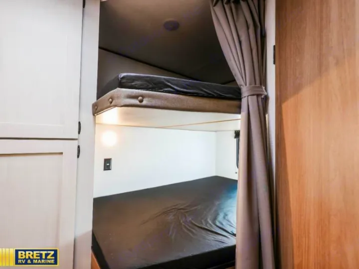 RV rental bunk beds: A compact sleeping area with two dark mattresses, a privacy curtain, and reading light. Ideal for family adventures.. Keystone RV Other 2026
