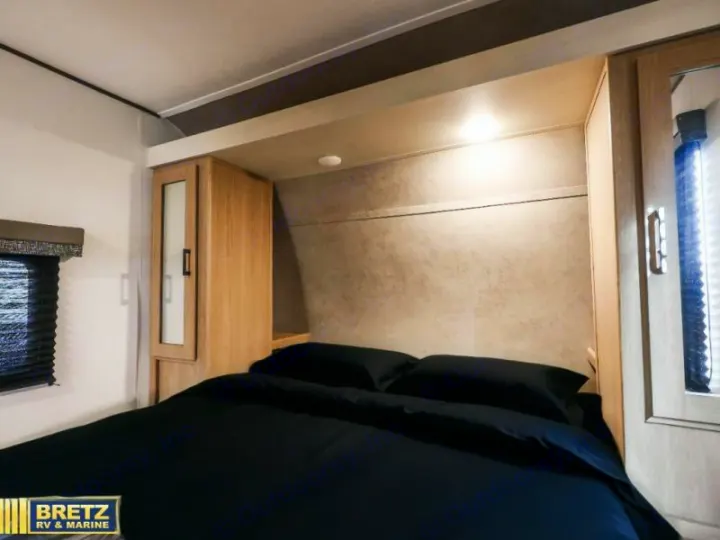 This modern rv rental bedroom features a comfortable bed, integrated overhead lighting, and wood-toned storage cabinets.. Keystone RV Other 2026