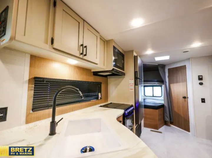 Modern kitchen in this RV rental offers a sink, stove, microwave, and cabinets. Bunk beds and a door are visible in the background.. Keystone RV Other 2026