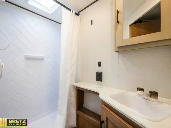 Clean RV rental bathroom featuring a white herringbone shower, vanity with sink, and mirror. Compact, bright interior for comfortable travel.. Keystone RV Other 2026