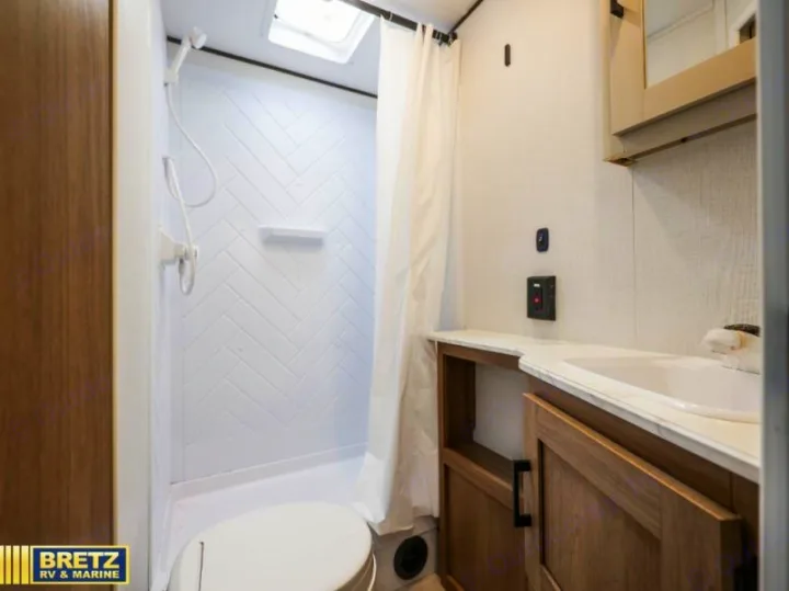 Experience comfort in this RV rental bathroom with a bright herringbone shower, toilet, and modern vanity with wood cabinets.. Keystone RV Other 2026