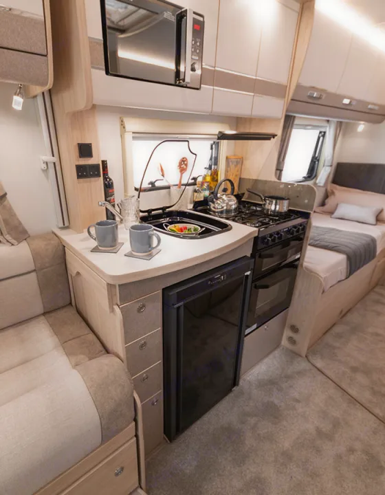 Modern RV rental interior featuring a compact kitchen with appliances, comfortable seating, and a cozy bed, perfect for travel.. Elddis Whirlwind GT 185 2026