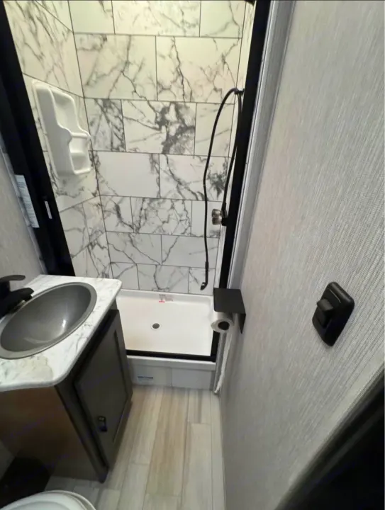 Inside this rv rental, a compact bathroom reveals a tiled shower, sink vanity with a metallic basin, and wood-look flooring.. Coachman Cross Trail 22xg 2023
