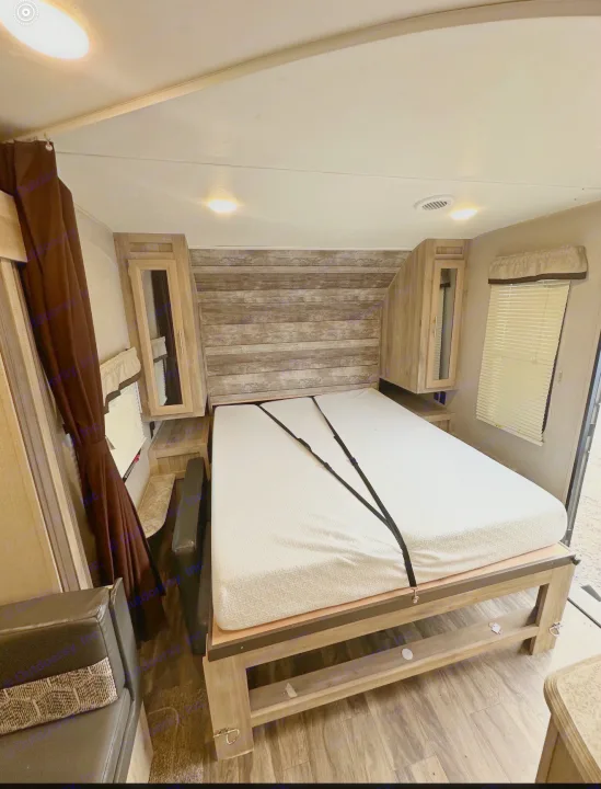 RV rental bedroom: a cozy interior featuring a patterned bed with security straps, overhead storage, and window blinds.. Coachmen 5ZT2CALB9LU036851 2020