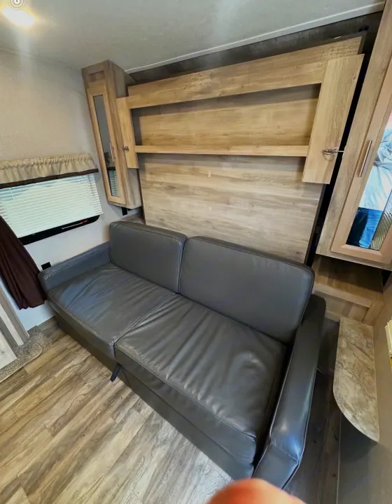 RV rental: Gray sofa, integrated wall unit with shelves and convertible bed, plus a window. Compact and functional living.. Coachmen 5ZT2CALB9LU036851 2020