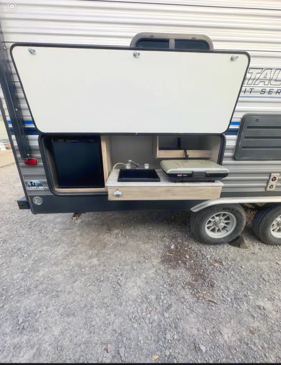 This RV rental's side view reveals a functional outdoor kitchen: mini-fridge, sink, and grill on a gravel surface.. Coachmen 5ZT2CALB9LU036851 2020