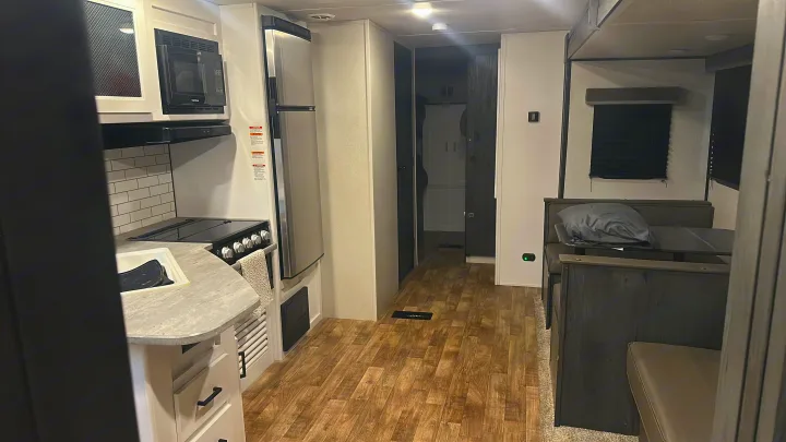 Modern rv rental interior: kitchen with white cabinets, subway tile backsplash, microwave, stove, fridge, and dinette.. Keystone RV Hideout 2022