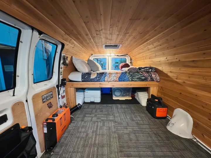 Inside an RV rental: a wood-paneled campervan with a bed, under-bed storage, portable heater, and power station.. Ford Econoline 150 1997