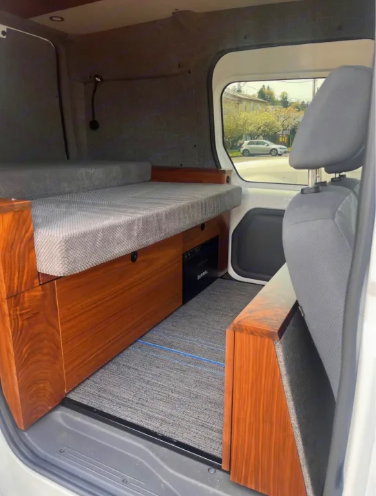Cozy RV rental interior with grey cushioned bed, sleek wood cabinetry, and integrated power unit for comfortable journeys.. Ford Transit 2013