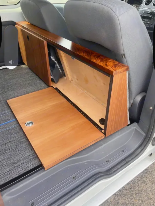 A custom-built wooden storage unit with an open compartment and a fold-down panel in an RV rental, positioned behind the front seats.. Ford Transit 2013