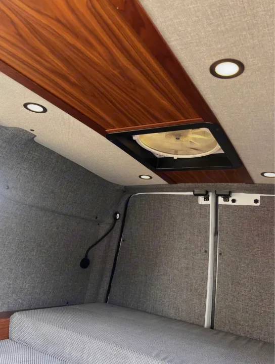 Sleek rv rental van interior featuring a warm wood ceiling, LED lights, a ceiling fan, and soft gray fabric walls/bed.. Ford Transit 2013