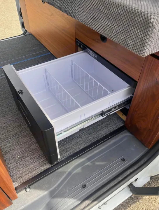 RV rental: Open drawer refrigerator with wire baskets in a modern camper van interior, featuring wood cabinets.. Ford Transit 2013