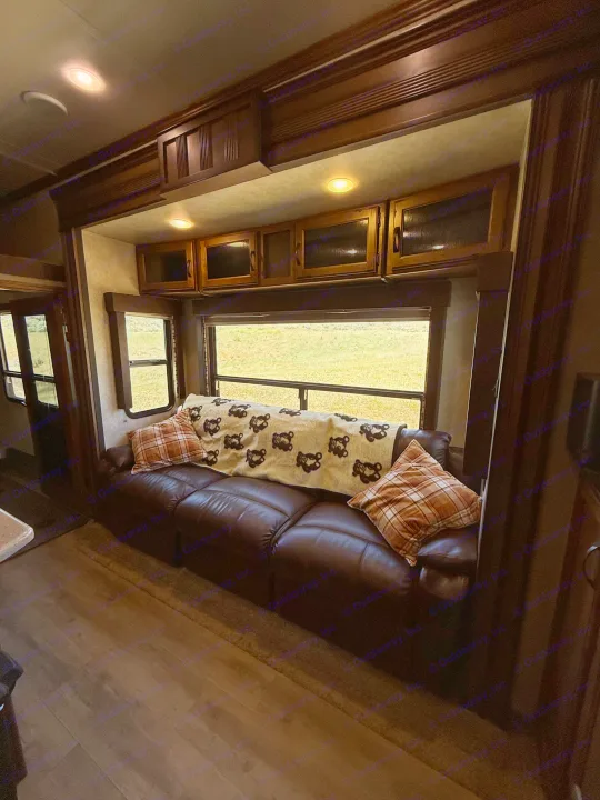 RV rental living area with a cozy leather couch, bear-patterned blanket, and scenic window view.. Keystone RV Carbon Toy Hauler 2015