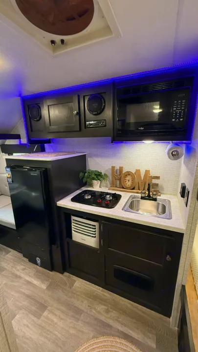 Inside an rv rental: a compact kitchen with microwave, fridge, stove, sink, dark cabinets, and blue LED accent lighting.. Braxton Creek Bushwhacker Plus 2024