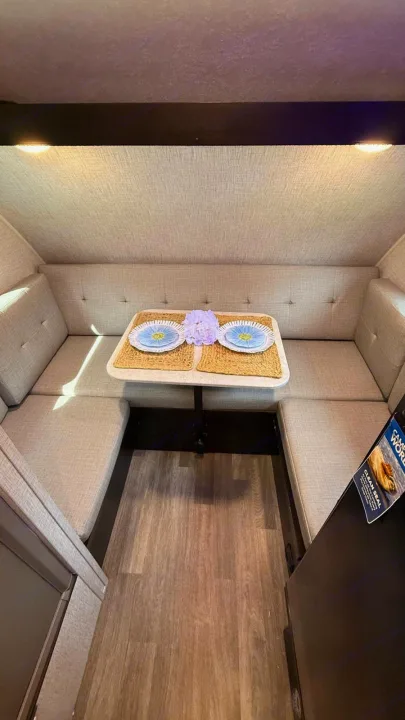 Modern RV rental dining booth with U-shaped seating, table set with blue plates & purple flowers, sleek wood-look floor.. Braxton Creek Bushwhacker Plus 2024