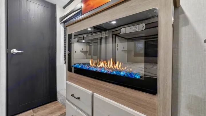 Experience comfort in this RV rental! Modern electric fireplace with blue glass, built into a cabinet next to a dark door.. Crossroads RV Cameo 2022