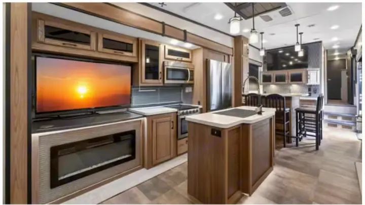 Spacious rv rental interior with wood cabinetry, modern kitchen, island, large TV, fireplace, and bar seating.. Crossroads RV Cameo 2022