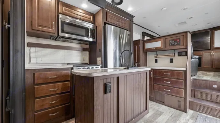 Spacious RV rental kitchen & living area with rich wood cabinets, stainless appliances, island, and a stepped living space.. Crossroads RV Cameo 2022