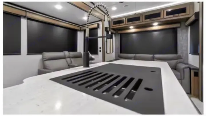 Modern rv rental interior, featuring a stylish kitchen island, black faucet, gray recliners, and overhead cabinets.. Crossroads RV Cameo 2022