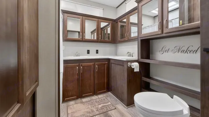 This RV rental bathroom features a double vanity, toilet, wooden cabinets, and a fun "Get Naked" sign.. Crossroads RV Cameo 2022