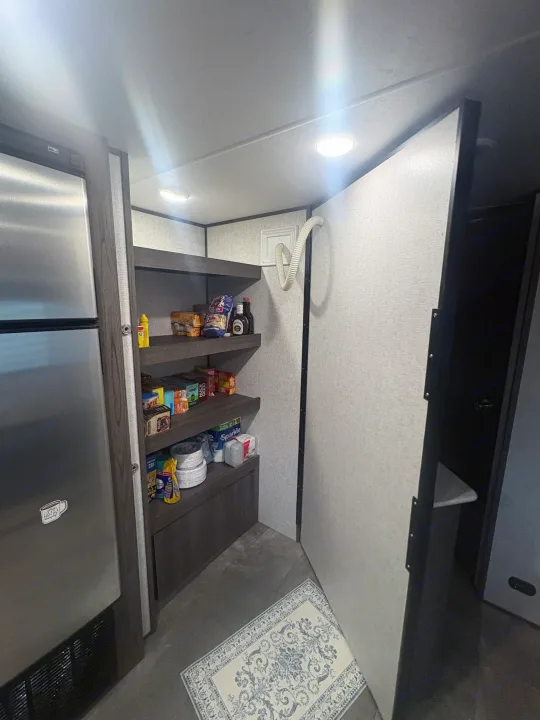 Inside an RV rental: a well-stocked pantry next to a stainless steel fridge, with shelving and a rug on the floor.. Dutchmen Kodiak SE 2021