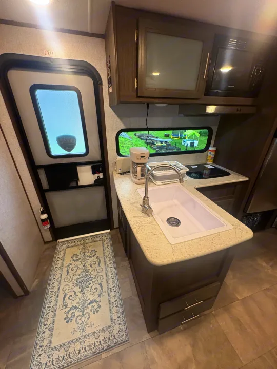RV rental's compact kitchen & entryway: white sink, coffee maker, toaster, microwave, and outdoor view from the window.. Dutchmen Kodiak SE 2021