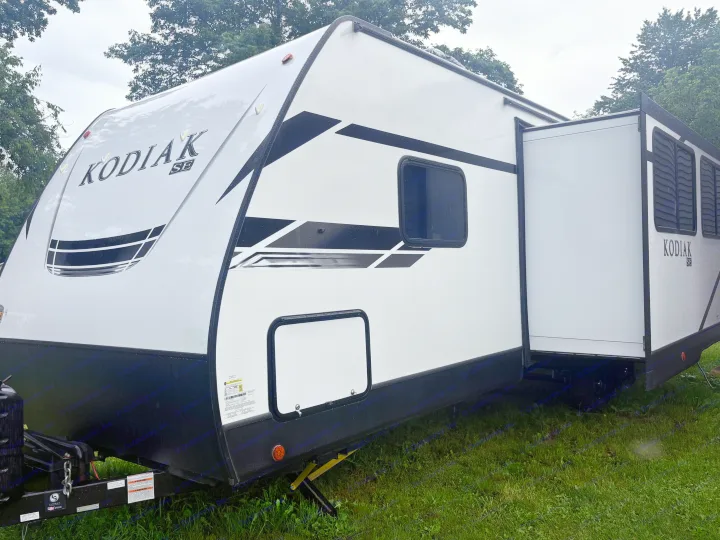 Kodiak SE travel trailer RV rental, white with black accents and extended slide-out, parked on green grass.. Dutchmen Kodiak SE 2021