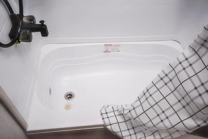 Inside an RV rental: a white shower/bathtub with a black faucet, drain, and plaid shower curtain.. Jayco Jay Flight SLX 2025