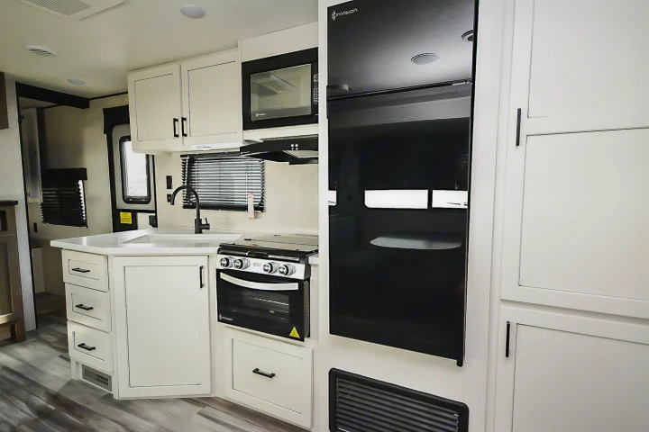 Modern rv rental kitchen with white cabinets, black appliances (fridge, microwave, oven), and sink.. Jayco Jay Flight SLX 2025