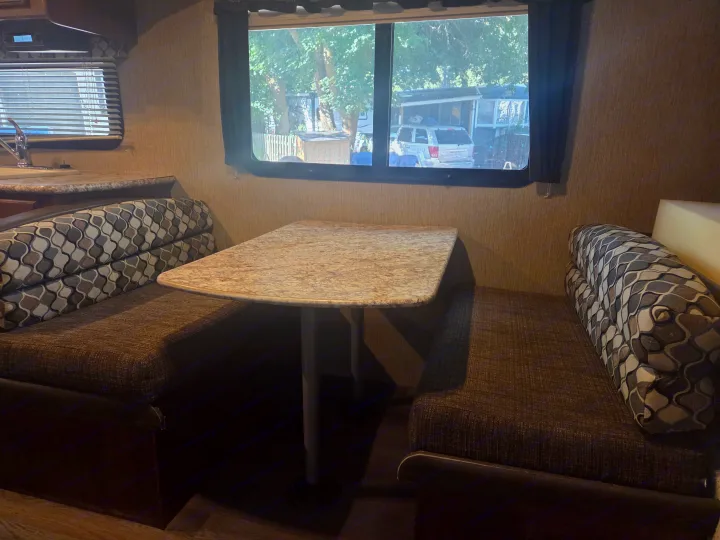 Cozy RV rental dinette featuring patterned cushions, a laminate table, and a view of a campground outside the window.. Keystone Outback 2017