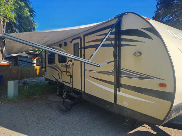 This Outback Ultra-Lite travel trailer for RV rental features an extended awning, parked outdoors on a sunny day.. Keystone Outback 2017