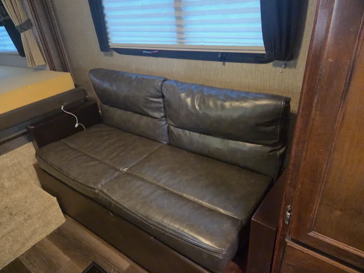 This cozy RV rental features a dark faux leather sleeper sofa, window with blinds, and a wooden cabinet.. Keystone Outback 2017